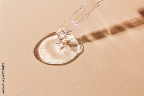 Transparent body serum flowing from a glass pipette front view.Cosmetic product close-up on a beige background. photo