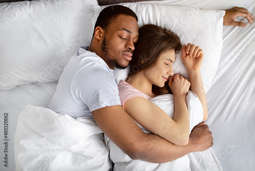 Top view of loving interracial couple sleeping in bed, hugging each other. Diverse love and relationships