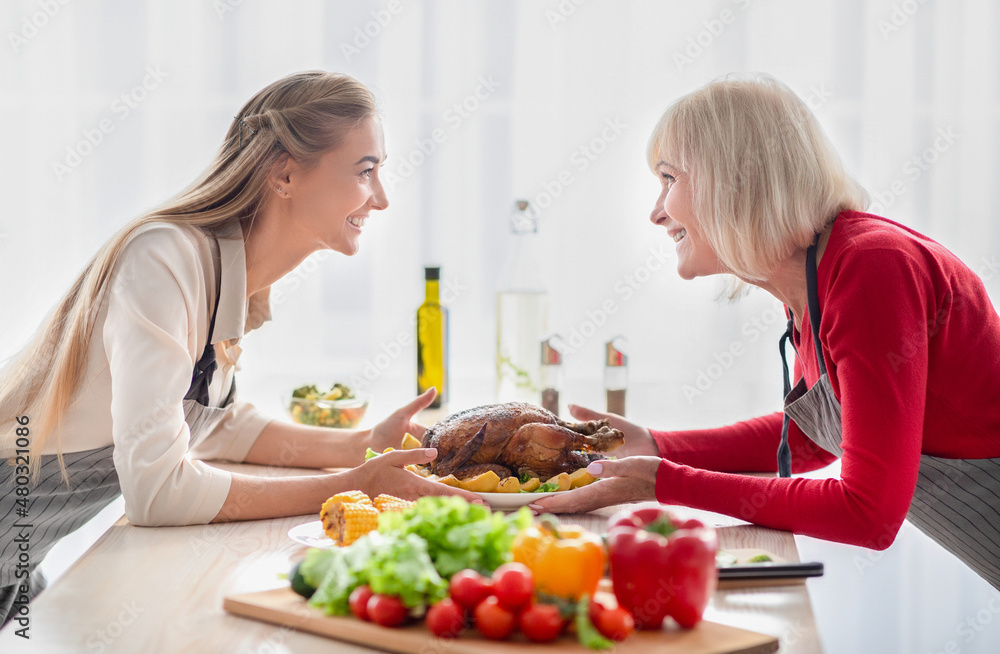 Happy young woman and her senior mother serving table with traditional festive turkey, having family holiday celebration Happy young woman and her senior mother serving table with traditional festive turkey, having family holiday celebration