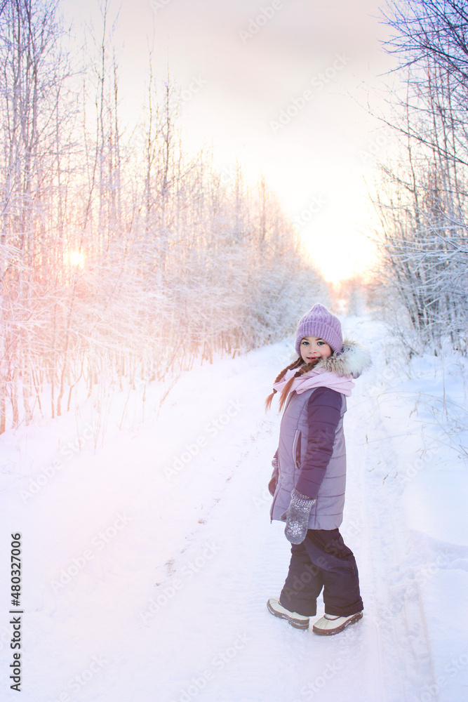 A girl stands on the road in the forest in the rays of the setting sun in winter A girl stands on the road in the forest in the rays of the setting sun in winter