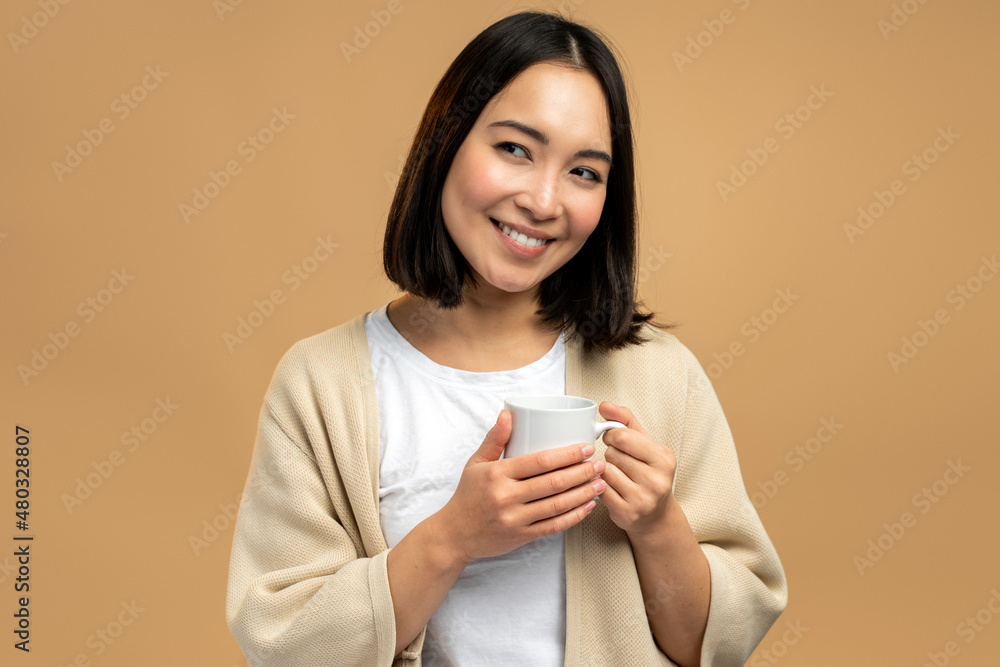 Charming asian female person holding cup with hot drink and looking away while posing Charming asian female person holding cup with hot drink and looking away while posing