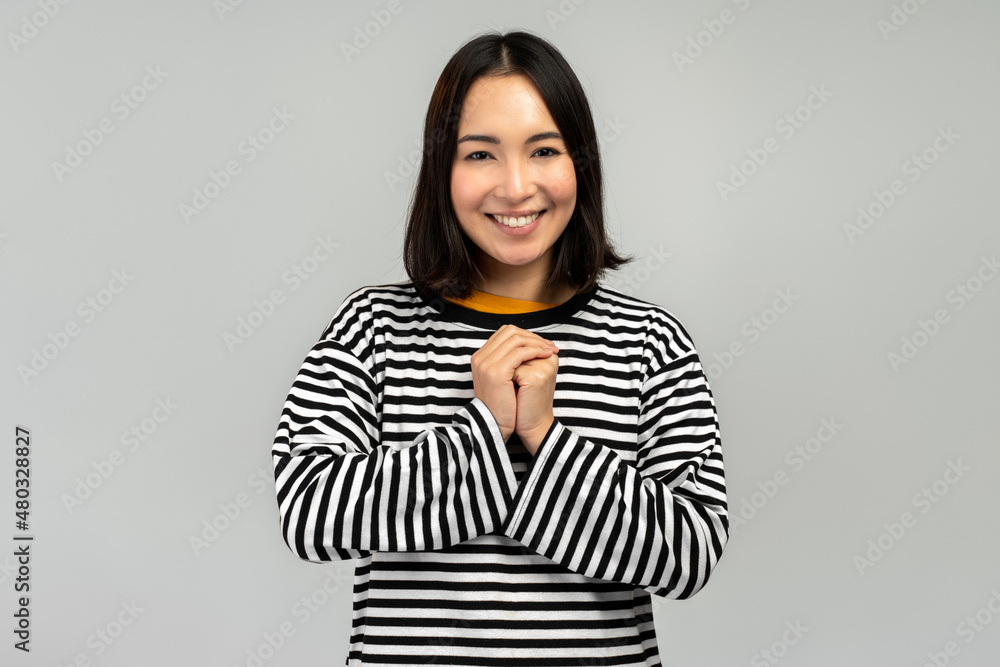 Happy asian young woman isolated on grey studio background holding hands near chest Happy asian young woman isolated on grey studio background holding hands near chest