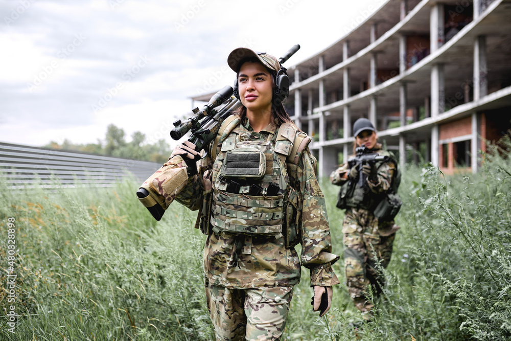 two strong ladies in tactical gear going in field, preparing for fight, war. Caucasian Military lady is Wearing gear uniform and automatic assault rifle. abandoned building in the background. two strong ladies in tactical gear going in field, preparing for fight, war. Caucasian Military lady is Wearing gear uniform and automatic assault rifle. abandoned building in the background.