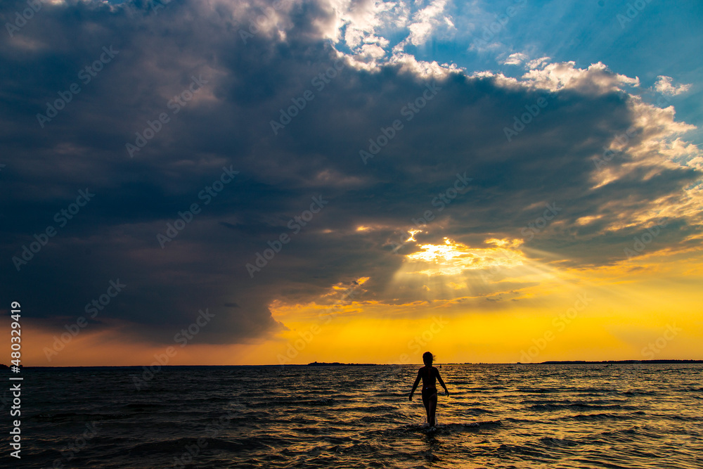 Teen Girl Walking in the Lake on Sunset Background.