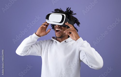 Funky Afro teen wearing VR headset, exploring cyberspace, using virtual reality for entertainment on violet background