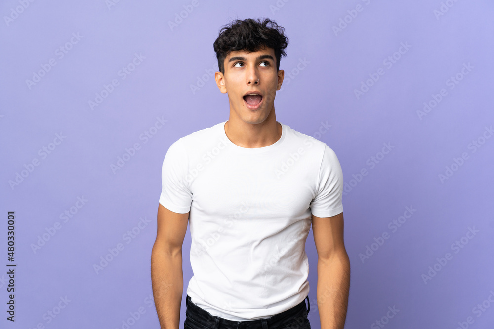 Young Argentinian man isolated on background looking up and with surprised expression Young Argentinian man isolated on background looking up and with surprised expression