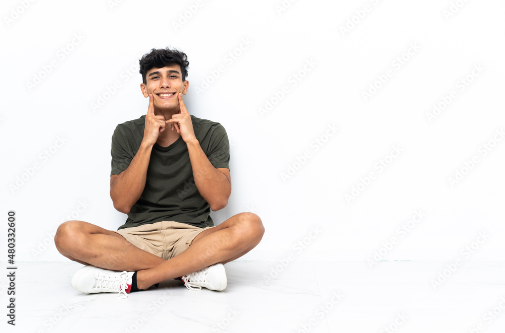 Obraz premium Young Argentinian man sitting on the floor smiling with a happy and pleasant expression