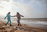 Happy family, mother and teenage daughter walking in the beach and have fun in wind weather in cold day