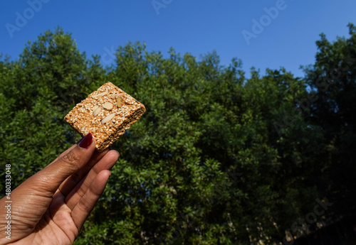 Til gajjak or Til sesame chikki in hand on nature background with trees and sky picnic food for Makarsankranti photo