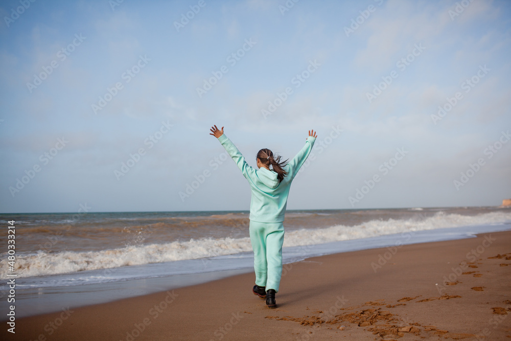 Teenager female walking outdoors in the beach in spring weather with wind, look to the sea, Girl dreased in blue hoody sweater and trousers Teenager female walking outdoors in the beach in spring weather with wind, look to the sea, Girl dreased in blue hoody sweater and trousers