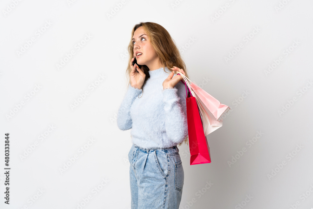 Young blonde woman isolated on white background holding shopping bags and calling a friend with her cell phone Young blonde woman isolated on white background holding shopping bags and calling a friend with her cell phone