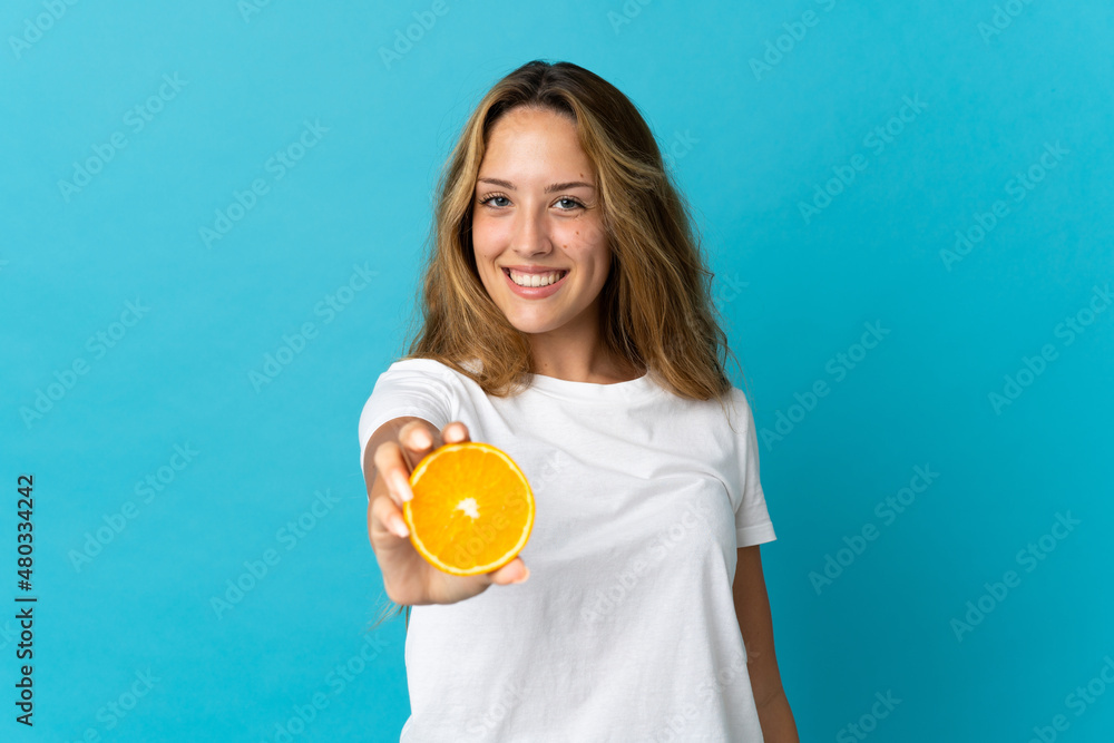 Young blonde woman isolated on blue background holding an orange Young blonde woman isolated on blue background holding an orange