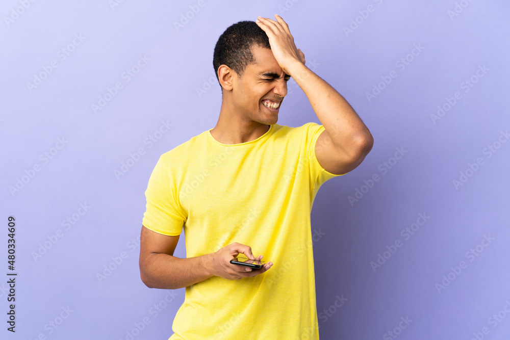 African American man over isolated purple background using mobile phone having doubts with confuse face expression African American man over isolated purple background using mobile phone having doubts with confuse face expression