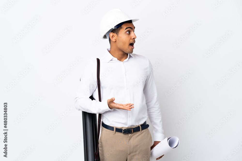 African American architect man with helmet and holding blueprints over isolated white background _ with surprise expression while looking side African American architect man with helmet and holding blueprints over isolated white background _ with surprise expression while looking side