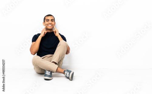 African American man sitting on the floor smiling with a happy and pleasant expression