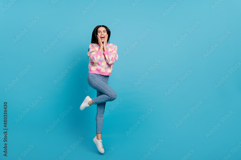 Photo of funny excited lady dressed print pullover arms cheeks jumping empty space isolated blue color background Photo of funny excited lady dressed print pullover arms cheeks jumping empty space isolated blue color background