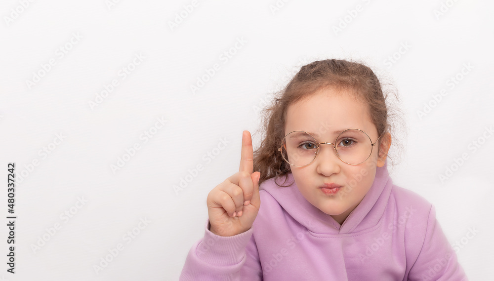 A girl of primary school age in glasses with her index finger raised up, close-up, isolates on a white background A girl of primary school age in glasses with her index finger raised up, close-up, isolates on a white background