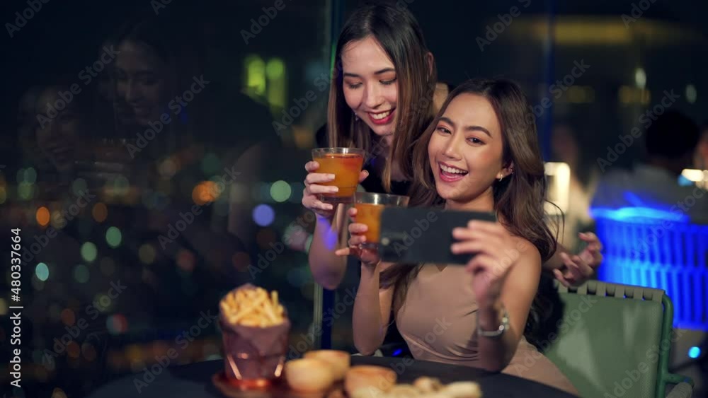 Asian woman friends in meeting and using smartphone selfie together while dinner at skyscraper rooftop restaurant in metropolis at night. Beautiful female enjoy outdoor lifestyle nightlife in the city Asian woman friends in meeting and using smartphone selfie together while dinner at skyscraper rooftop restaurant in metropolis at night. Beautiful female enjoy outdoor lifestyle nightlife in the city