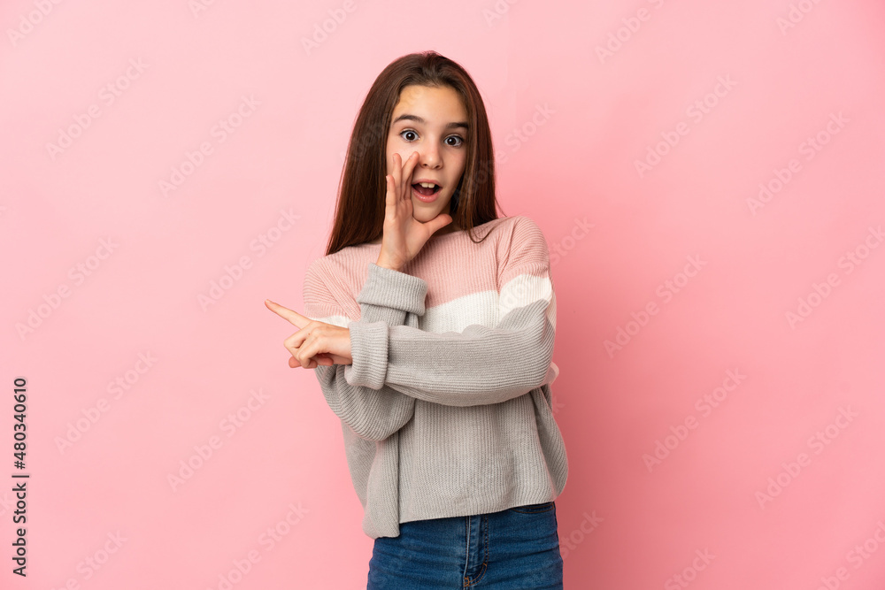 Little girl isolated on pink background pointing to the side to present a product and whispering something Little girl isolated on pink background pointing to the side to present a product and whispering something