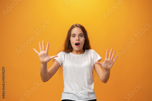 Scared young teen girl showing stop gesture against yellow background