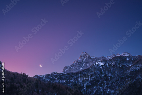 Crescent waning moon in purple sky overy mountain peaks