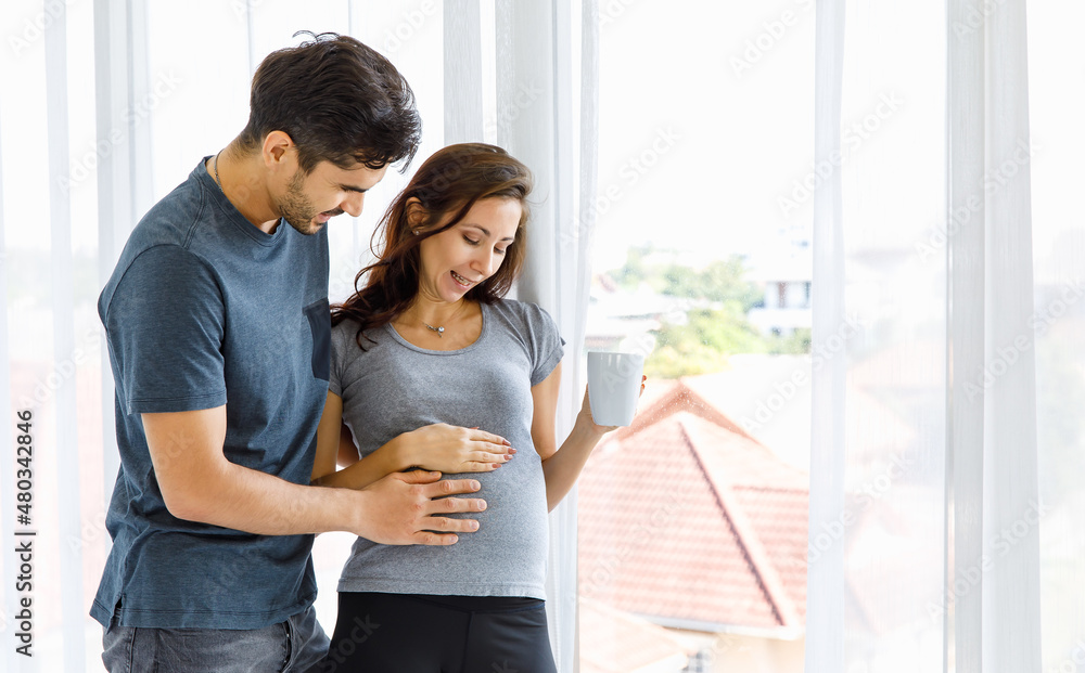 Father tenderly embracing beloved wife and touching belly of unborn baby while motherhood drinking glass of milk for pregnancy nourishment Father tenderly embracing beloved wife and touching belly of unborn baby while motherhood drinking glass of milk for pregnancy nourishment