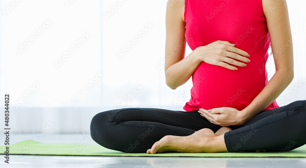 Obraz premium Caucasian pregnant woman close eyes, tenderly touch belly, and quietly sit on yoga floor mat for calmly meditation and mindfulness practice as maternity exercise for healthy unborn baby.