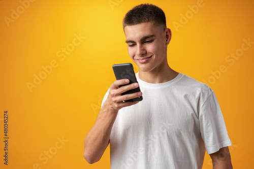 Young casual man teenager using a smartphone against yellow background