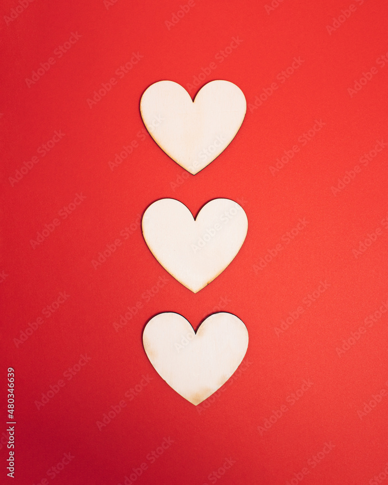 Tree wooden natural hearts centered on bright red background. Sharing valentine getting in love atmosphere. Minimal flat lay concept for holiday romance.