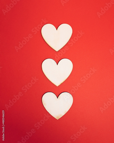 Tree wooden natural hearts centered on bright red background. Sharing valentine getting in love atmosphere. Minimal flat lay concept for holiday romance.