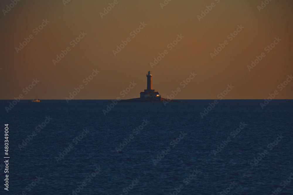 Silhouette of a lighthouse and boat on the ocean sea waters.