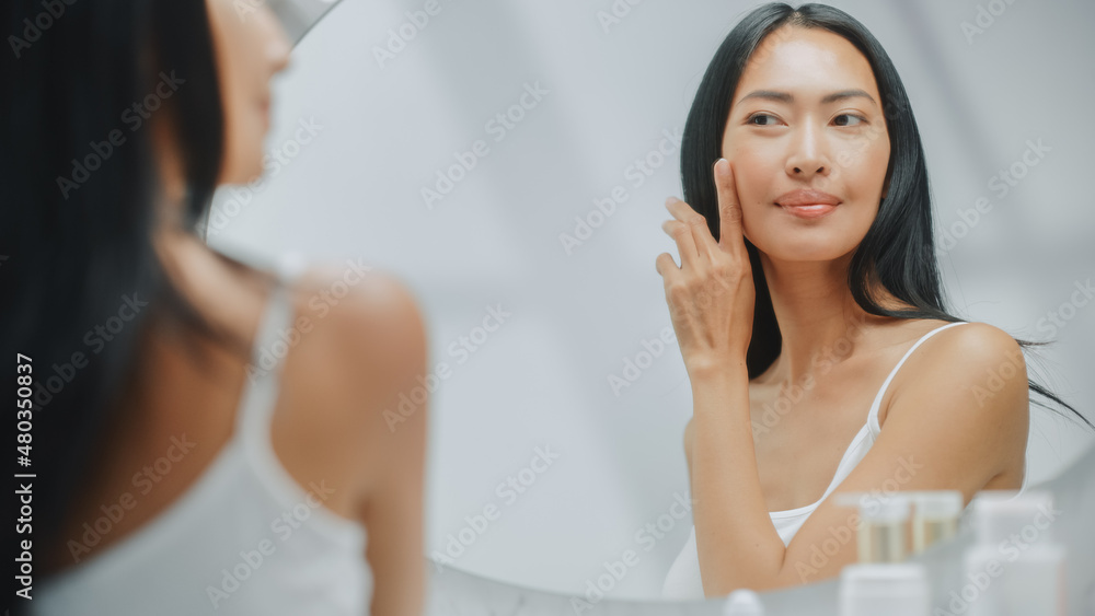 Beautiful Asian Woman Touches Her Perfect Soft Skin and Lush Black Hair, Smiles in the Bathroom Mirror. Concept for Healthy Wellbeing, Natural Beauty, Organic Skincare Products Beautiful Asian Woman Touches Her Perfect Soft Skin and Lush Black Hair, Smiles in the Bathroom Mirror. Concept for Healthy Wellbeing, Natural Beauty, Organic Skincare Products