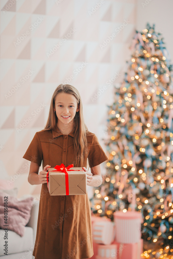 Back view of kid holds a gift box near the Christmas tree indoors. Back view of kid holds a gift box near the Christmas tree indoors.