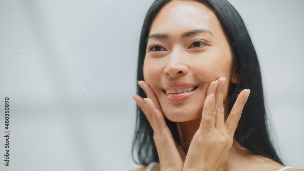 Beautiful Asian Woman Touches Perfect Soft Face Skin, Applies Advanced Organic Cream, Smiles in the Mirror. Happy Female Enjoying Her Beauty Routine. Wellbeing, Natural Cosmetic Products. Close-up Beautiful Asian Woman Touches Perfect Soft Face Skin, Applies Advanced Organic Cream, Smiles in the Mirror. Happy Female Enjoying Her Beauty Routine. Wellbeing, Natural Cosmetic Products. Close-up