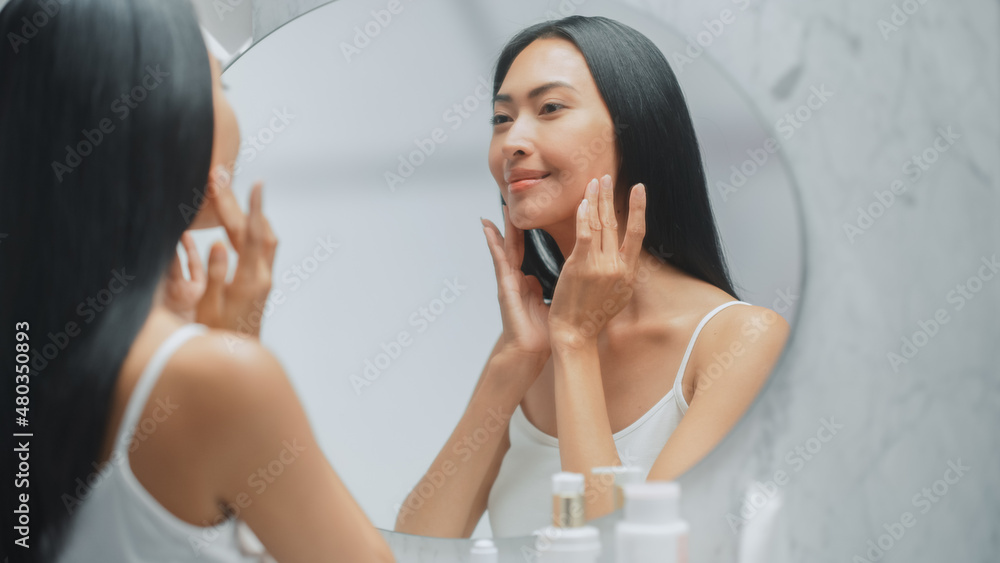 Beautiful Asian Woman with Perfect Soft Face Skin, Uses Advanced Organic Cream, Smiles in the Mirror. Happy Female Enjoying Her Beauty Routine. Wellbeing, Natural Cosmetic Products. Close-up Portrait Beautiful Asian Woman with Perfect Soft Face Skin, Uses Advanced Organic Cream, Smiles in the Mirror. Happy Female Enjoying Her Beauty Routine. Wellbeing, Natural Cosmetic Products. Close-up Portrait