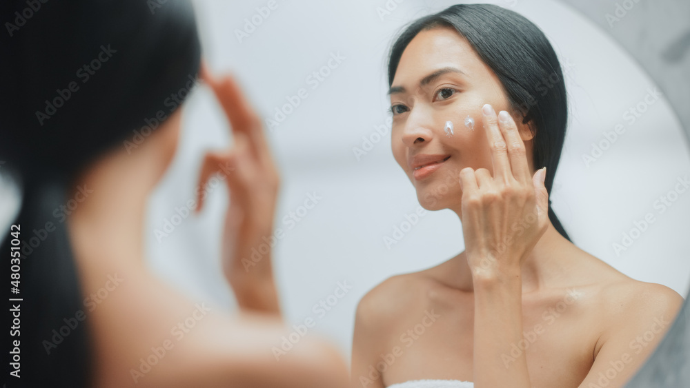 Portrait of Beautiful Asian Woman Gently Applying Face Cream Mask with Sensual Touches, Looking in Bathroom Mirror. Young Female Makes Her Skin Soft, Clean with Natural Cosmetics Skincare Product Portrait of Beautiful Asian Woman Gently Applying Face Cream Mask with Sensual Touches, Looking in Bathroom Mirror. Young Female Makes Her Skin Soft, Clean with Natural Cosmetics Skincare Product