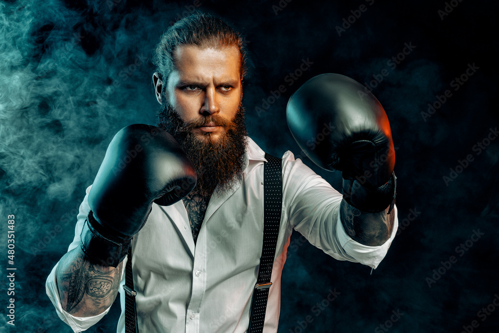 Serious bearded man in white shirt wears boxing gloves and ready to fight in smoke. Man self defense