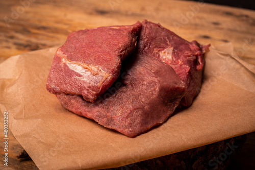 Raw game meat, beef. Pieces of meat on parchment paper, on wooden background. High quality roe, deer, fallow deer meat.