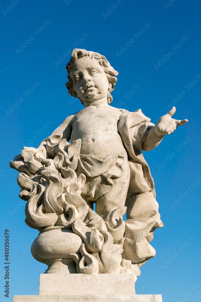 Putto angel statue in white stone against blue sky, symbolic sculpture with flame