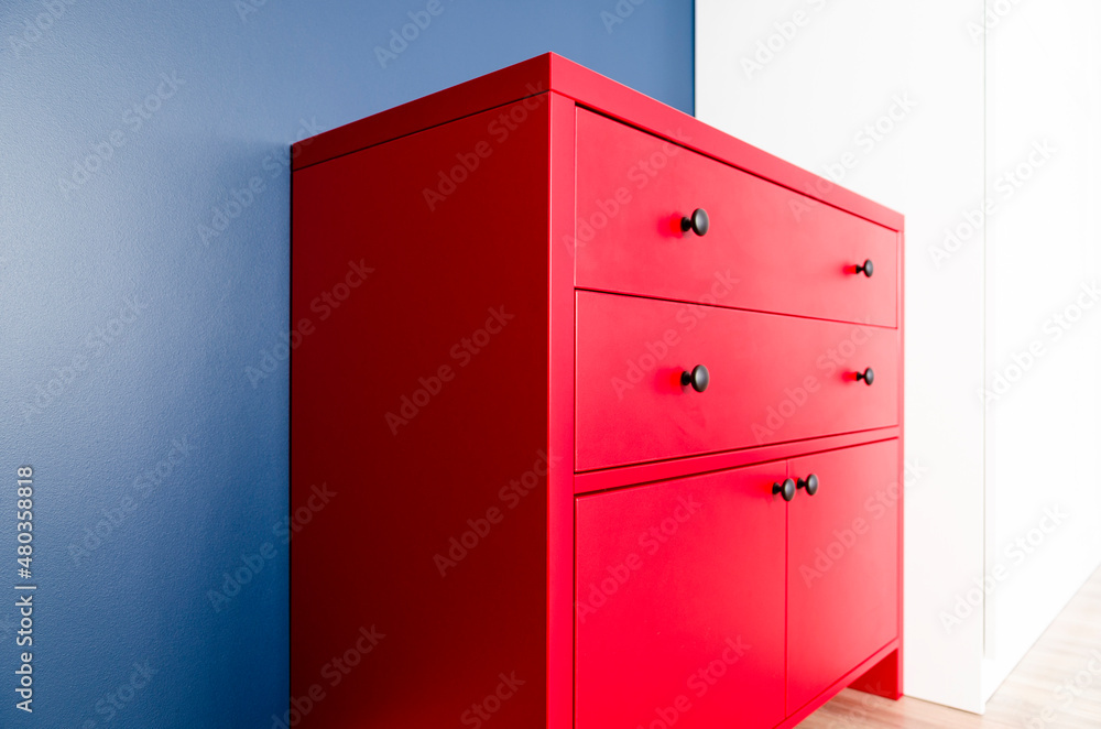 Interior design. Red wooden chest of drawers in Scandinavian style against a blue wall Interior design. Red wooden chest of drawers in Scandinavian style against a blue wall