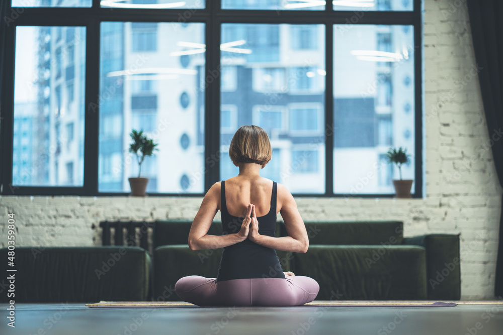 Woman Sitting in Lotus Pose and Meditating with Open Hands. Yoga Female Practicing Yoga Meditation Exercise on the Mat in her Living Room at Home. Close-up Woman Sitting in Lotus Pose and Meditating with Open Hands. Yoga Female Practicing Yoga Meditation Exercise on the Mat in her Living Room at Home. Close-up