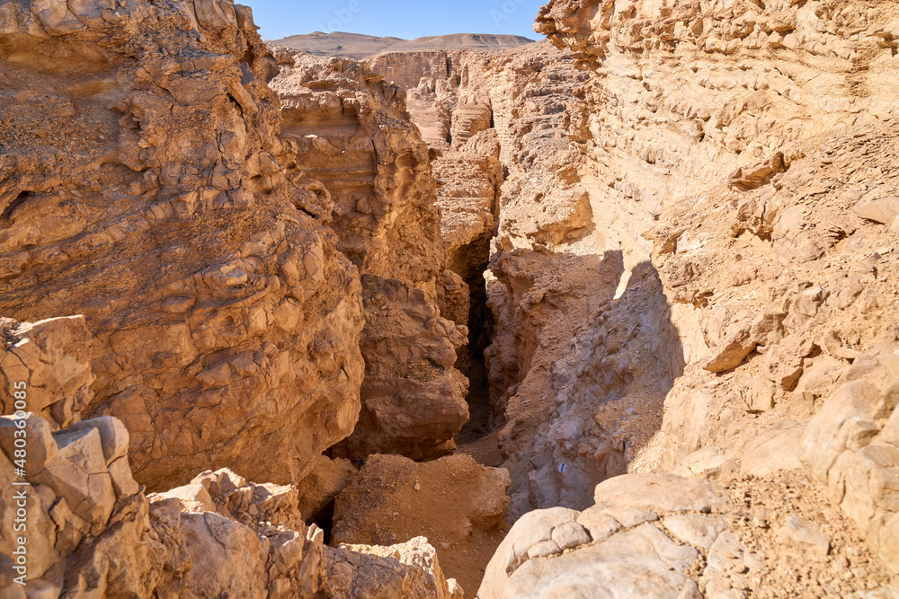Hiking trail descending into a deep dark gorge inside a dry canyon in a remote desert region. High walls of a narrow canyon of wadi Hava in the Negev Desert.