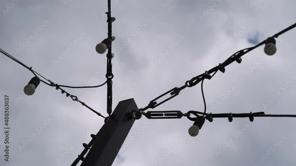 Garlands of light bulbs are fixed with different metal carabiners on a black pillar. View of the mount up the sky with clouds. Garlands of light bulbs are fixed with different metal carabiners on a black pillar. View of the mount up the sky with clouds.