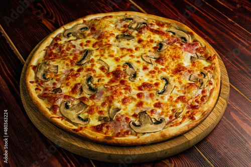Mushroom and ham pizza with cheese and tomato sauce on a wooden tray and table.