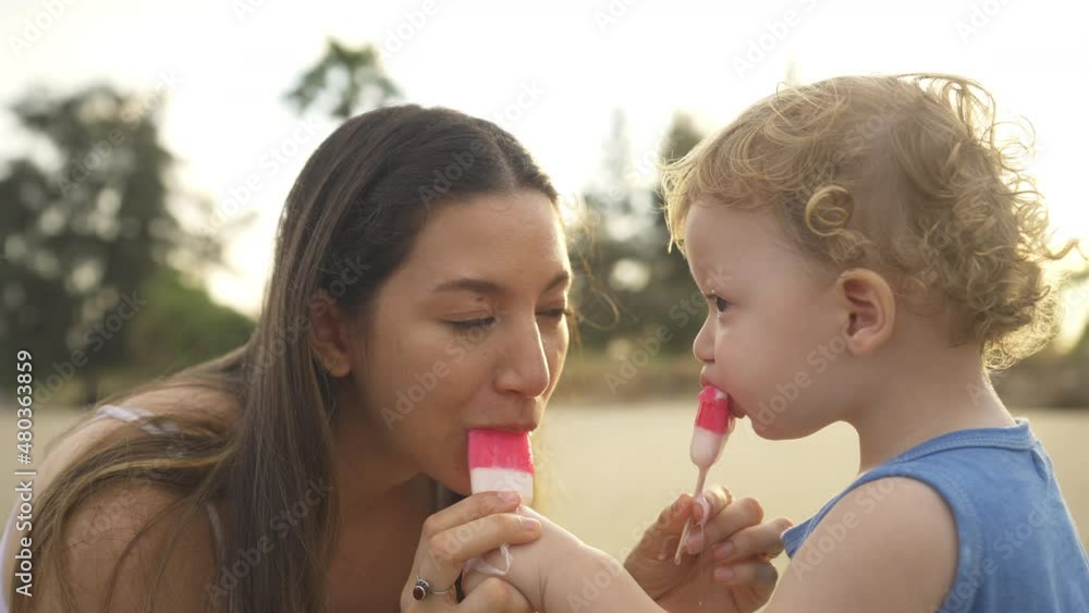Caucasian mother with cute baby son eating ice cream together on tropical beach in sunny day. Happy family parent with little child boy kid enjoy outdoor lifestyle activity on summer travel vacation Caucasian mother with cute baby son eating ice cream together on tropical beach in sunny day. Happy family parent with little child boy kid enjoy outdoor lifestyle activity on summer travel vacation