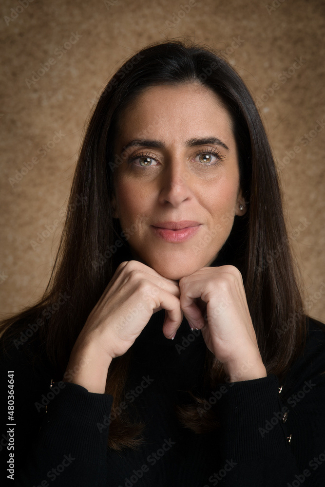 Retrato de joven mujer atractiva mirando a la cámara, con las manos juntas debajo de la barbilla, con un fondo marrón desenfocado y jersey negro. Retrato de joven mujer atractiva mirando a la cámara, con las manos juntas debajo de la barbilla, con un fondo marrón desenfocado y jersey negro.