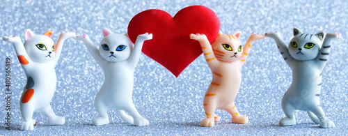 Four funny toy kittens and a big red heart on a light shiny background. The concept of family relationships, congratulations on valentine's day or wedding anniversary and family life.