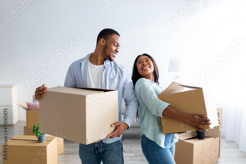 Home relocation concept. Loving african american couple carrying carton boxes in their new house, copy space