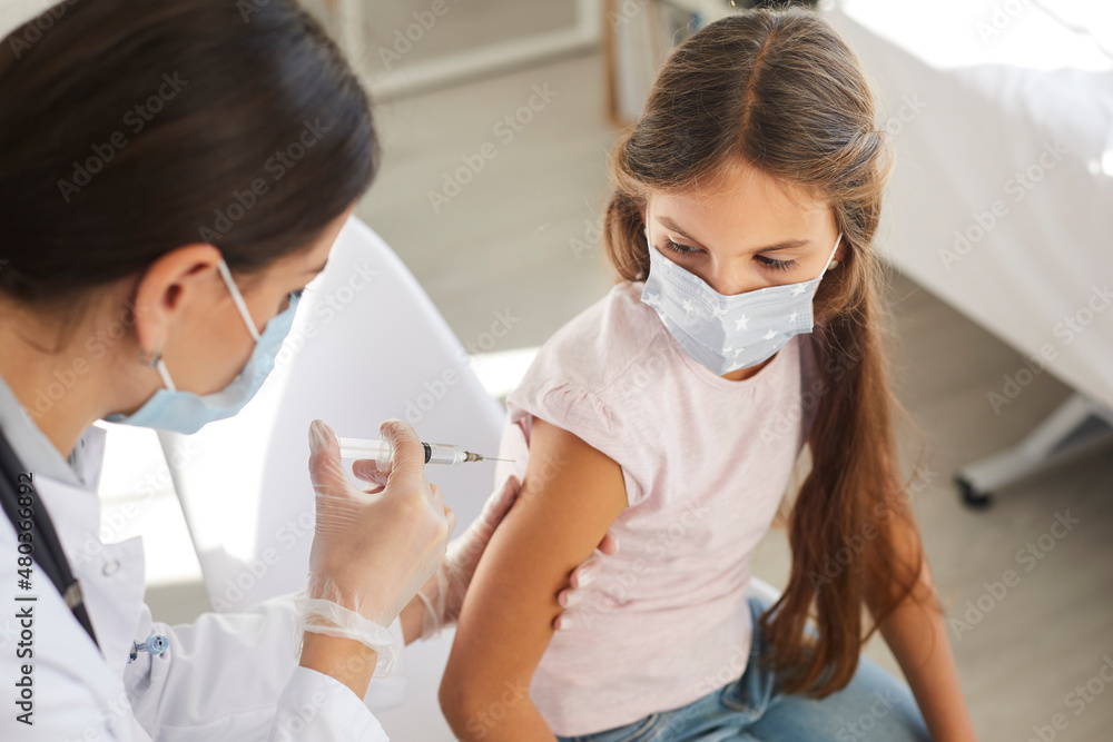 Female nurse in white gloves holding syringe and giving new effective vaccine to child. Doctor at modern clinic gives flu or Covid 19 shot to little kid. Close up. Vaccination and immunization concept