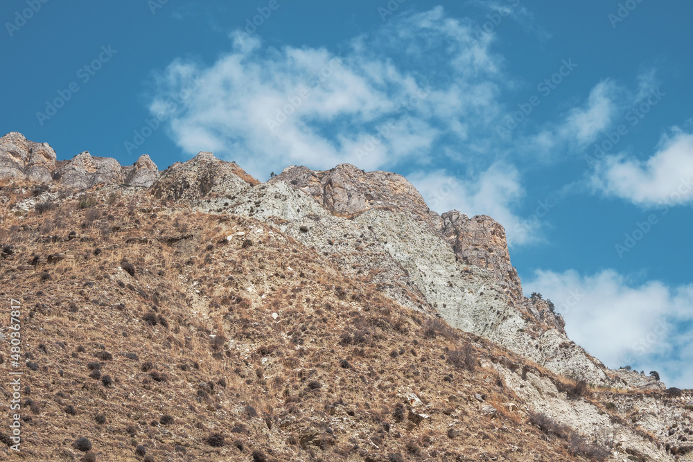 Minimalistic atmospheric landscape with rocky mountain wall with pointy top in sunny light. Loose stone mountain slope in the foreground. Sharp stony mountains.